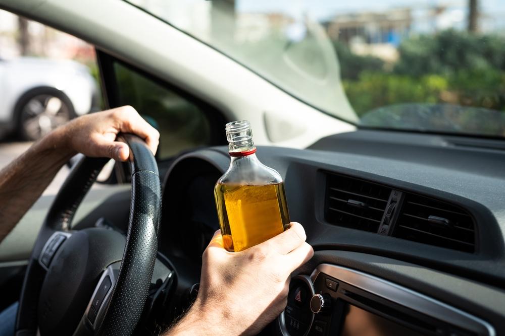 Man holding a bottle of alcohol while driving a car