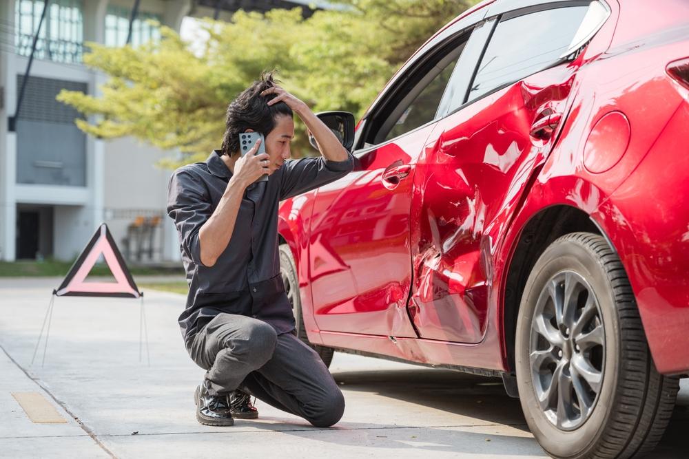 A man clutching his head as he stares at his damaged car. Learn about how Uber handles accidents.