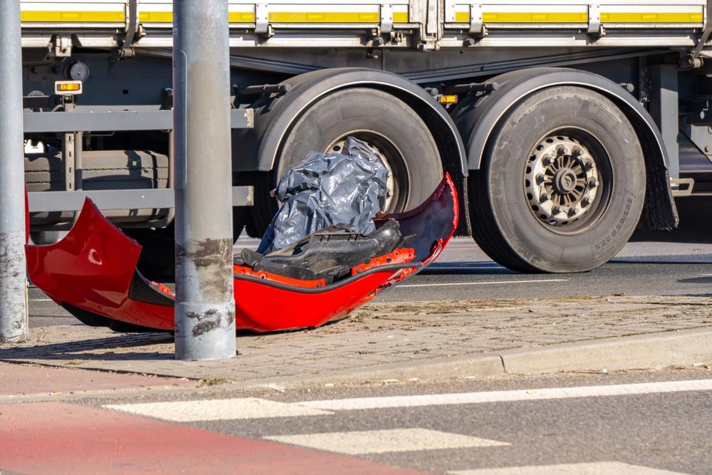red car bumper lying on the sidewalk after a road collision with a truck