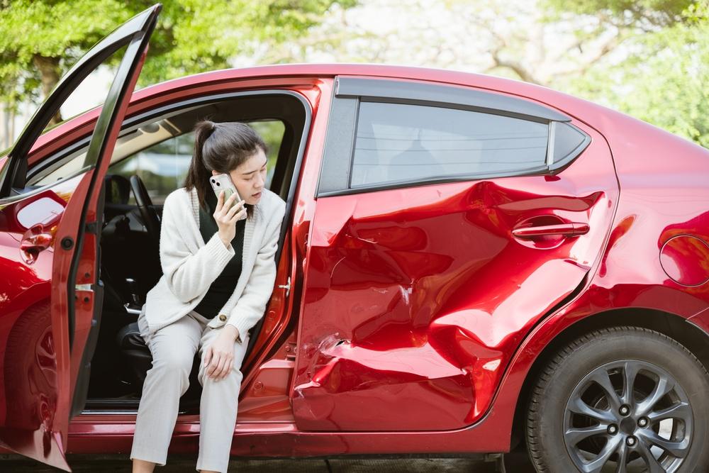 woman is sitting in a red car with a smashed front end