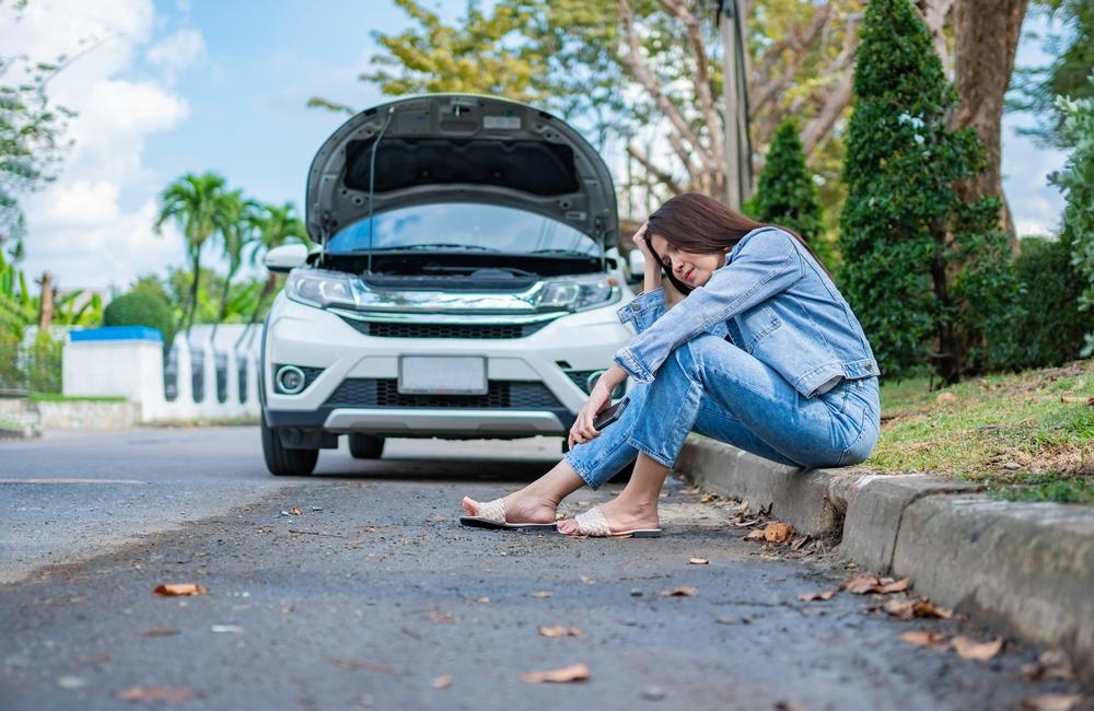 woman sitting beside car after a car breakdown on street
